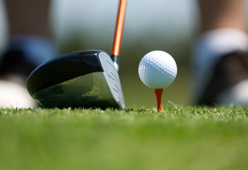 Up close image of a golf ball on tee with club. An up close image of a golf club next to a ball on tee
